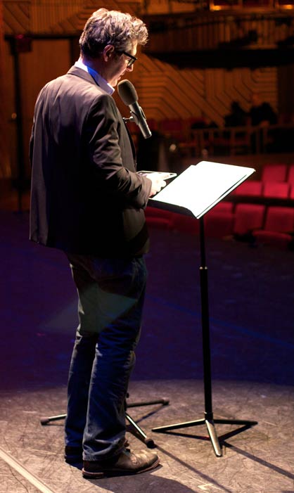 Image of Ira Glass reading from a podium in a recording session of This American Life